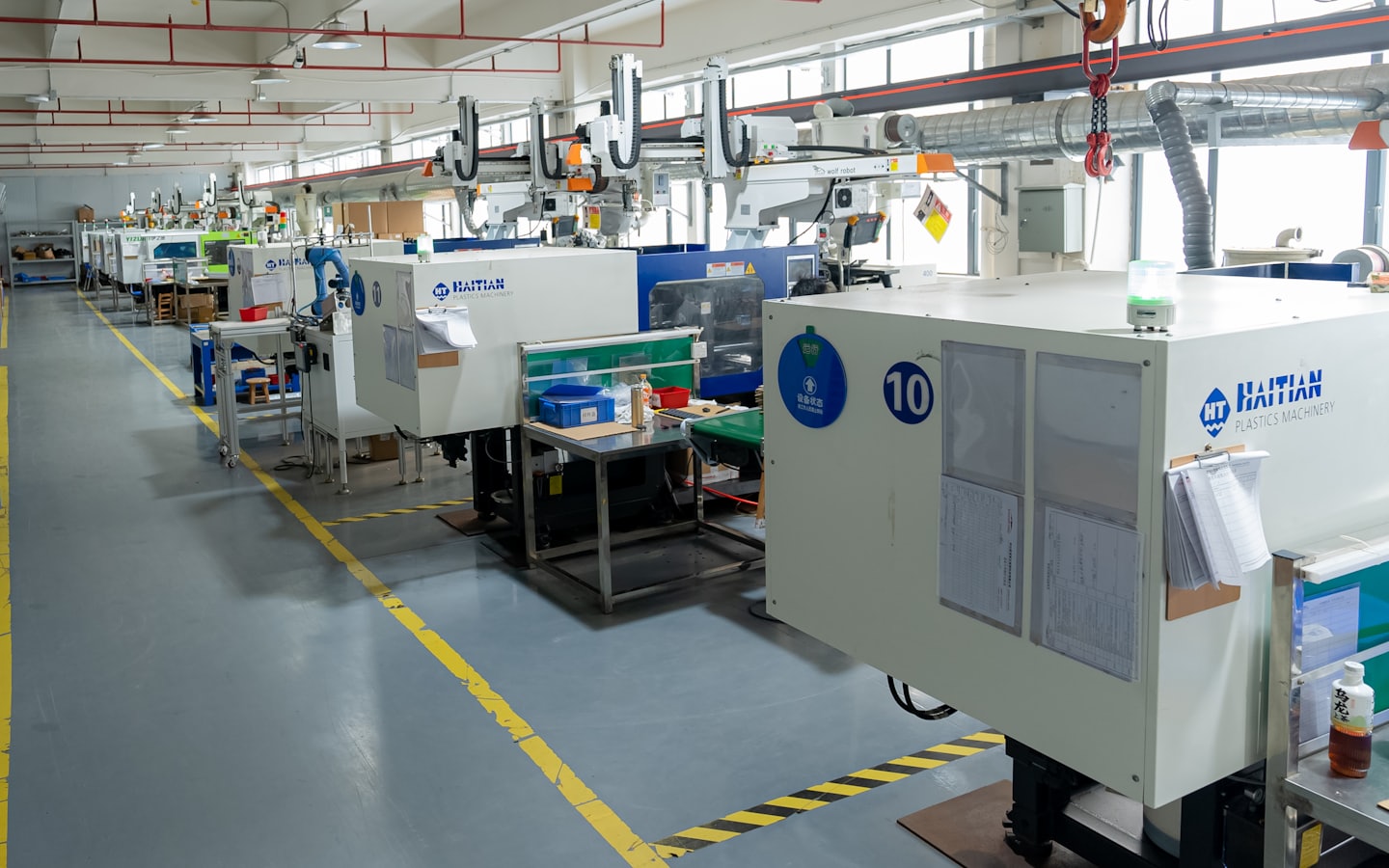 Robotic arms operate on plastic molding machines in a factory.