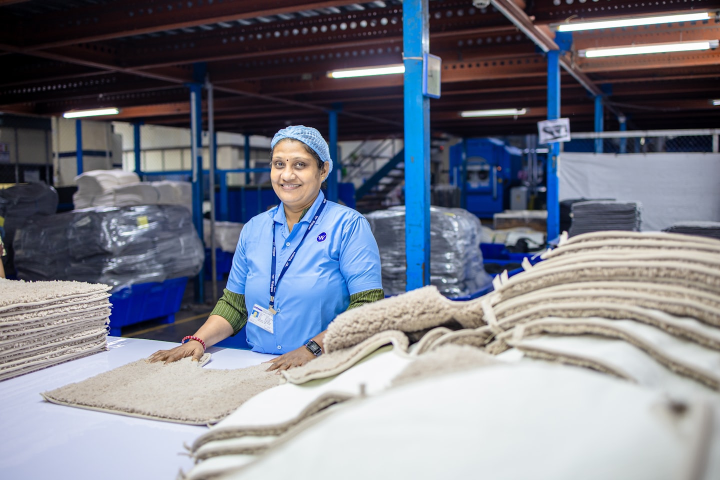 Factory worker inspects beige floor mats on a long table.