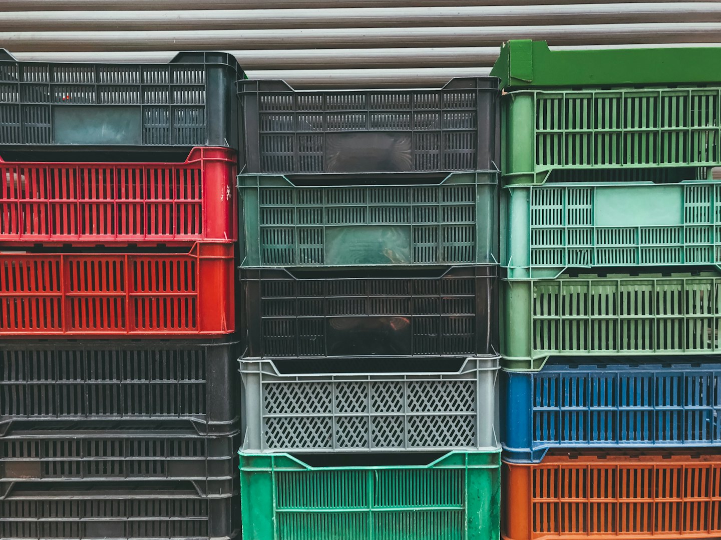 Multi-colored plastic crates stacked against a beige roller door.